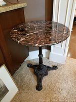 Full view of small round marble top table with polished marble and detailed cast iron base.