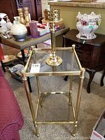 Brass and glass side table with brass candle stick holder on top, showing full table and items around it