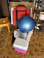 Full view showing red folding tables and chairs in background, exercise ball and cooler in foreground, and other items stacked