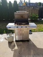 Full front view of the Char-Broil stainless steel gas BBQ grill with open lid and propane tank on left side.