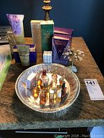 Overview photo of miniature perfume bottles in metal tray, full-size boxed perfumes, lotion tubes, and semi-precious stone tree on countertop.