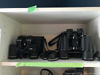Three binoculars on a shelf, showing carrying cases and straps.