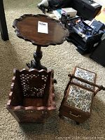 Wide shot showing the small wood pedestal table, carved wood plant holder, and wooden sewing kit with floral padded upholstery and drawer.