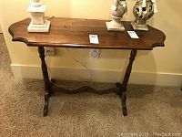Full view of the wooden sofa or entrance table showing scalloped edge top and turned legs.