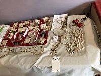 Wide view of assorted earrings pinned on cards and laid out on a red velvet tray next to several necklaces and bracelets on a beige cloth.