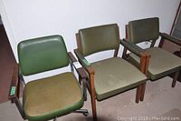 Front view of three office chairs showing the green fabric seat and vinyl back of the swivel chair and the two matching wooden chairs