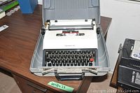 Front view of portable typewriter in gray carrying case open on brown wooden desk