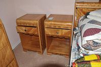 Two matching solid wood side tables placed side by side, showing fronts with drawer and open shelf space, light wood finish.