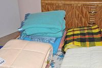 Various sheep wool duvets and blankets stacked on bed with wooden headboard and dressers in background