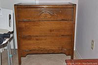 Front angle view of wooden dresser showing the carved decorative detail on the top drawer and overall condition.