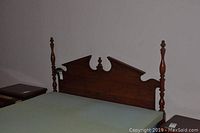 Wooden bed with carved headboard and spindle footboard, mattress on frame.