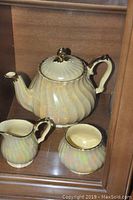 Ceramic swirled teapot along with matching creamer and sugar bowl on a wooden shelf.