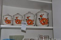 Four ceramic canisters with orange floral design on a shelf