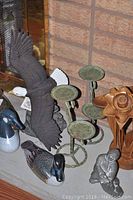 Close-up photo focusing on metal eagle sculpture with wings expanded, two duck figurines, rustic metal candle holders and wooden flower sculpture