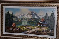 Front view of framed signed landscape painting showing mountain, lake, cabin and trees