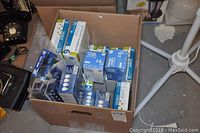 Photo showing a cardboard box filled with assorted new light bulbs in various branded packages.