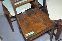 Close-up image of one wooden chair seat showing wood grain and wear, with a green sticker showing dimensions 17x16x33 inches.