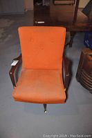 Front view of vintage orange swivel rocker chair with wooden armrests.