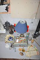 Photo shows all items grouped on the floor: blue shade table lamp, horse head sculpture, colorful tin box, wooden trays, small ceramic container, key, and various trinkets.