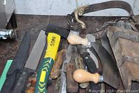 Overview of all knives, ax, sharpening stones and gloves laid on a table.