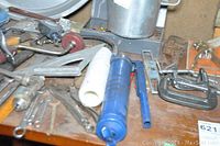 Angle showing assortment of tools on wooden surface, including blue grease gun and clamps