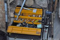 Photo showing yellow tackle box with multiple fishing lures and tackle, fishing rods, and fishing reel.