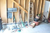 Wide view showing wooden ladder, a variety of garden tools including shovels, rakes, hand tools, and multiple stacked garden planters and pots.