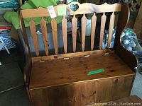 Front view of wooden deacons bench showing hinged seat and spindle back with heart cutout.
