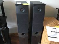 Front view of two Energy e:XL series floor-standing speakers with black fabric grille and wooden finish base.