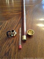 Disassembled walking stick showing wooden shaft, small glass shot glass, small glass container, and brass top.