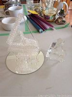 Shannon crystal grand piano with intricate texture, shown on a reflective round base, next to a smaller clear glass piano figurine placed on a white surface with various household items in background.
