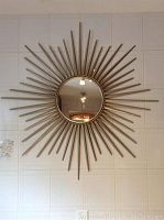 Metal sunburst style round mirror hanging on wall showing radiating metal rods and circular mirror center.