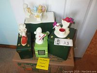 4 Snowbabies figurines displayed on their original green and yellow boxes with handwritten labels, arranged against a white door.