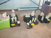 Overview of multiple Snowbabies figurines arranged on boxes and carpet, including gingerbread house, children in various poses dressed in winter coats and hoods.