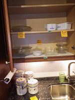 Kitchen cabinet shelf with five Blue Cornflower ceramic canisters with metal clip lids on countertop and various glass bowls and baking dishes on shelves above.