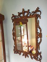 Front view of the rectangular ornate resin framed mirror showing detailed floral and scroll designs on the brown frame reflecting room interior.