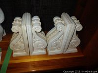 Front view of both pairs of white decorative bookends with scroll and leaf designs.