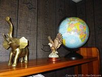Brass elephant figurine, eagle figurine, and globe arranged on a wooden shelf