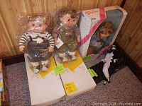 Photo of 2 Amy's Child Association dolls in original packaging and 1 Precious Playmates porcelain clown doll with damaged box on carpeted floor.