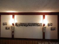 Wide view showing the set of five metal music-themed wall decor pieces mounted on a textured white wall. Two smaller pieces on each side and largest long piece in center.