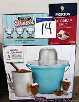 Photo showing boxed Nostalgia electric ice cream maker with blue 4 quart tub and stainless steel paddle, boxed set of four glass dessert bowls, and box of Morton ice cream salt.