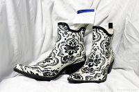 Side view of the black and white floral patterned cowboy rain boots placed on a white fabric background.