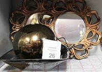 Two bronze-colored ornate wall-mounted mirrors and a water fountain basin with a reflective metallic dome and rocks, including a power cord and pump visible.