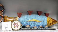 Front view of the large metal fish-shaped candle holder painted blue and yellow with five triangular candle holders on top