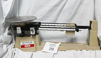 Photo of vintage OHAUS three beam balance scale showing the full length of the scale with metal base, sliding weights, and round stainless steel weighing pan.