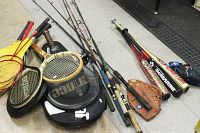 Photo showing fishing rods, tennis racquets with cases, assorted baseball bats, mitts and gloves on floor