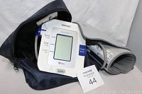 Omron blood pressure machine with cuff and blue carrying case visible, showing digital display and control buttons.