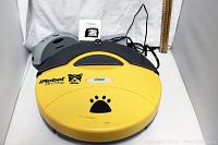 Yellow iRobot Roomba Dirt Dog robotic vacuum with visible scuffs and paw print graphic, sitting next to grey charging dock with power cord attached.