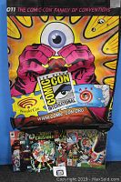 Photo of large colorful San Diego Comic Con 2011 tote bag with graphic artwork and comic books beneath it including X-Men and Mighty Crusaders.