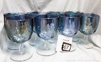 Group of 8 vintage iridescent blue glasses on white fabric background, showing their rounded shape and reflective blue coloring.